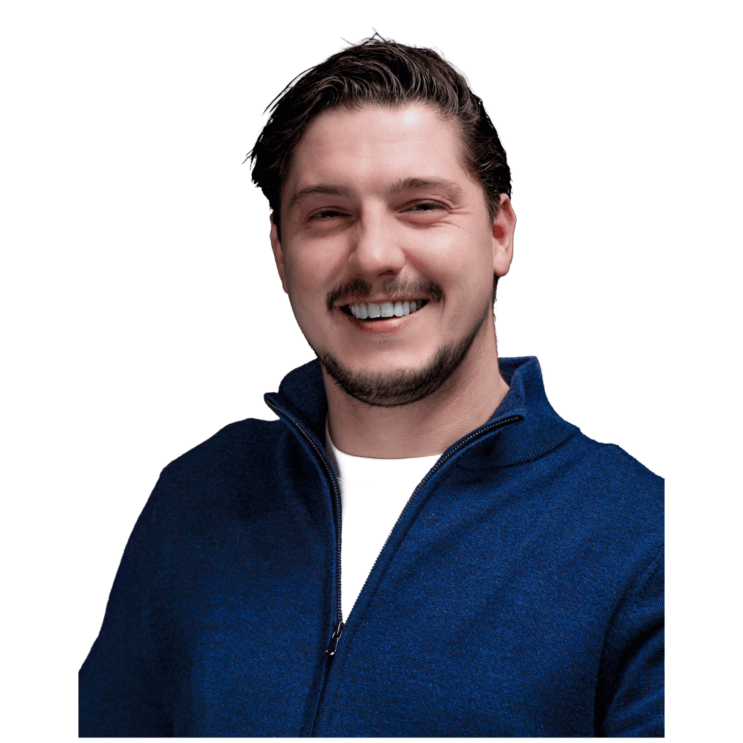 Een man met kort donker haar en een getrimde baard, die een blauwe trui met ritssluiting over een wit overhemd draagt, glimlacht naar de camera tegen een effen witte achtergrond, waaruit vertrouwen in cyberbeveiliging en beveiligingsbewustzijn blijkt.